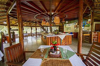 Restaurant der Turtle Lodge im Amazonas in einem offenen hölzernen Pavillon. In der Mitte steht ein Büffet auf einem Holztisch mit weißem Tischtuch.
