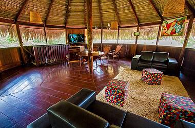 Lounge-Pavillon der Turtle Lodge in Brasilien mit schwarzen Ledersofas, bunten Sitzwürfeln, Holzstühlen und einem Fernseher